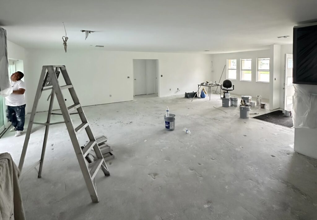 New construction painting in progress inside a modern open-plan home with primed walls, ladder setup, and interior finishing underway